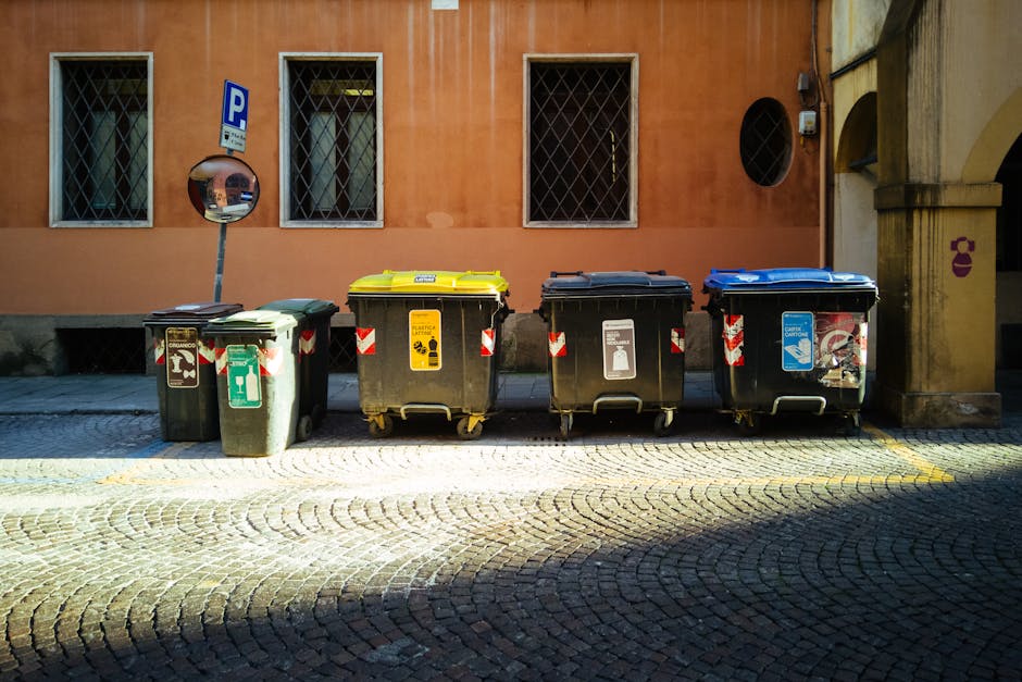 A close-up view of a pile of crumpled aluminum food and beverage cans, including some with visible brand labels such as Coca-Cola, scattered across a surface. The cans vary in size and color, with sil